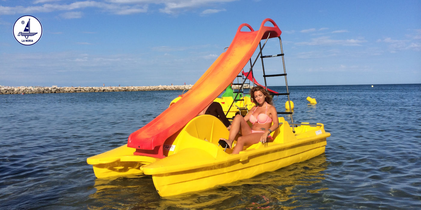mujer en bikini disfrutando un hidropedalo amarillo con tobogán en la costa de Estepona