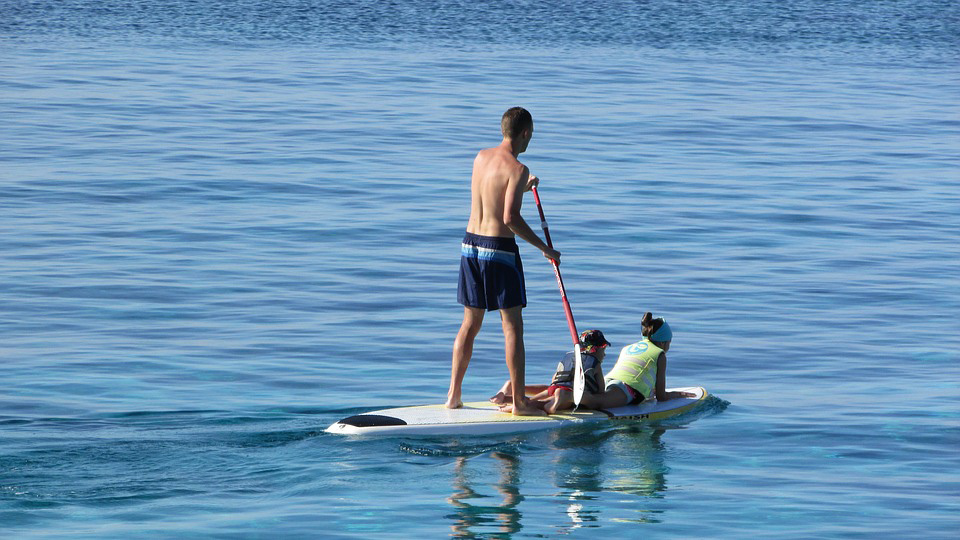 hombre practicando paddle surf con dos niños sobre la tabla en aguas tranquilas